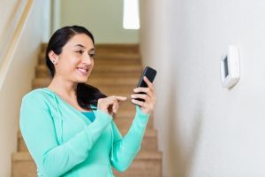 person-adjusting-smart-thermostat-with-phone